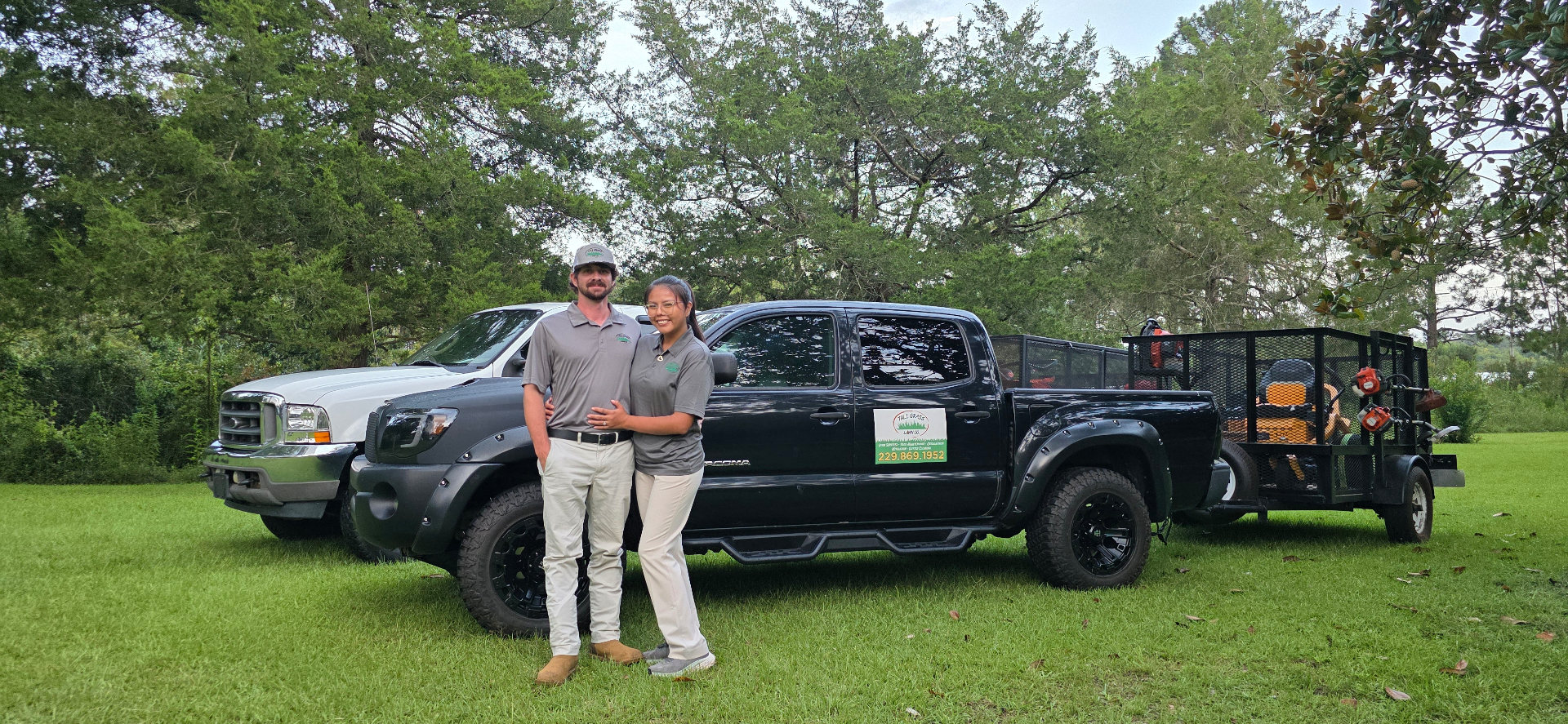 Owners of Tall Grass Lawn Co. standing in front of their work truck and trailer